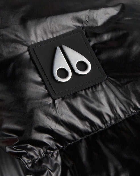 Close-up of a black glossy jacket with a black square patch featuring two silver, abstract, antler-like shapes.