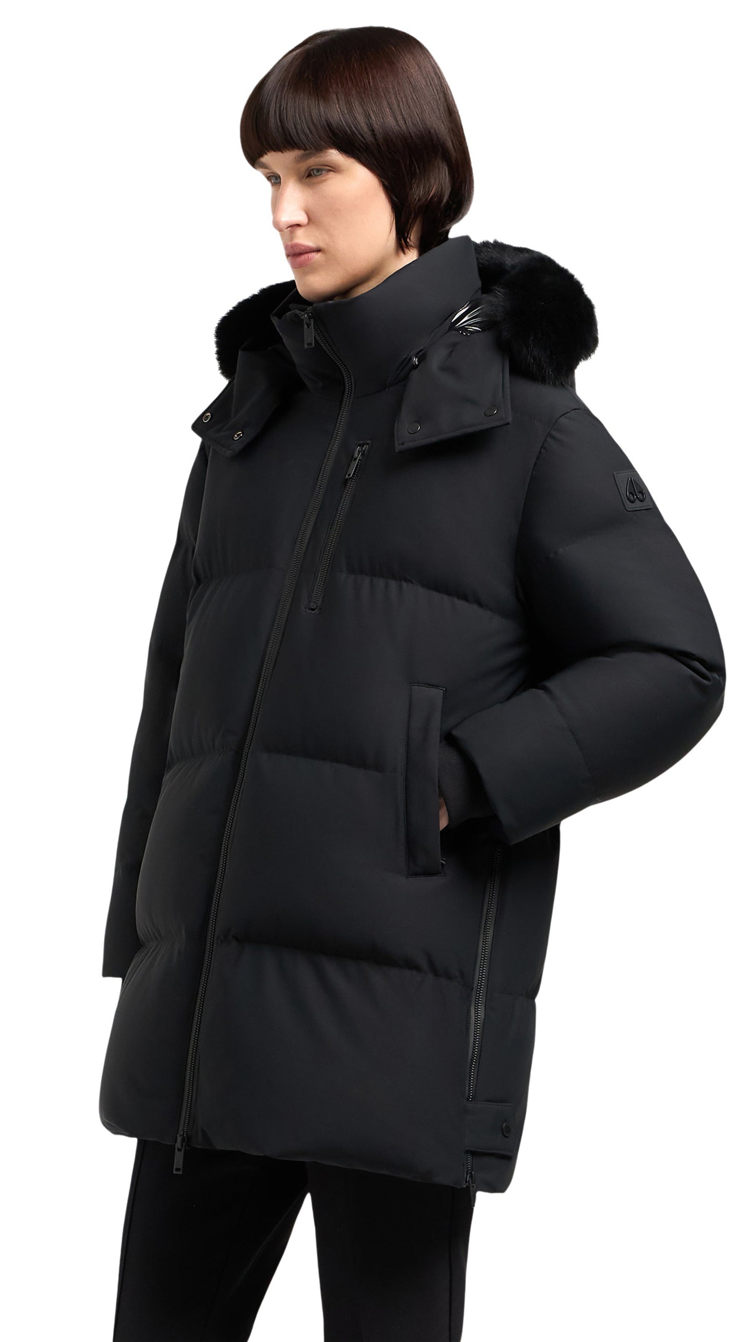 A person wearing a long, black puffer jacket with a fur-trimmed hood, the jacket features a zip closure and pockets.