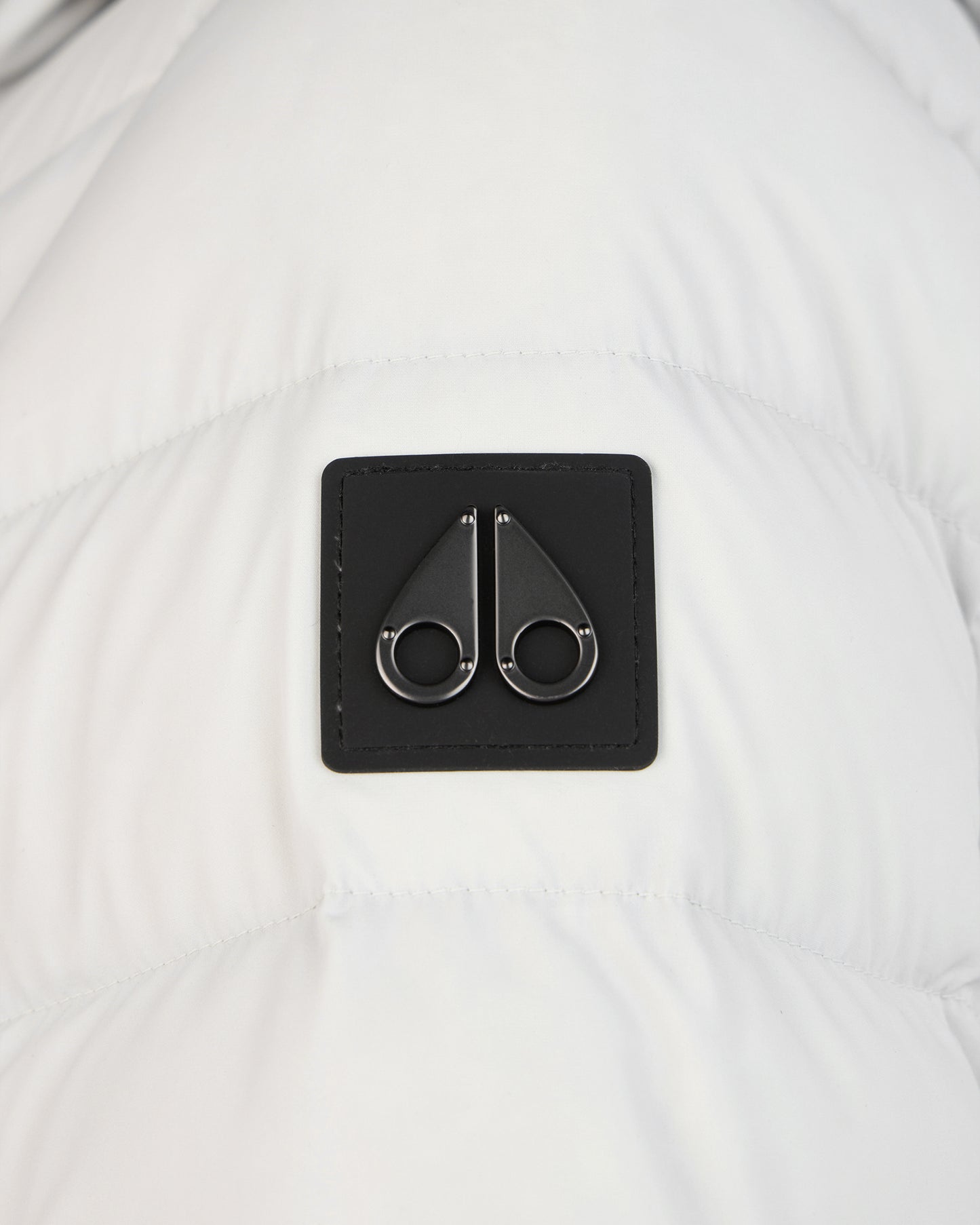 Close-up of a black, square-shaped logo with two metallic rings attached to the top and bottom.