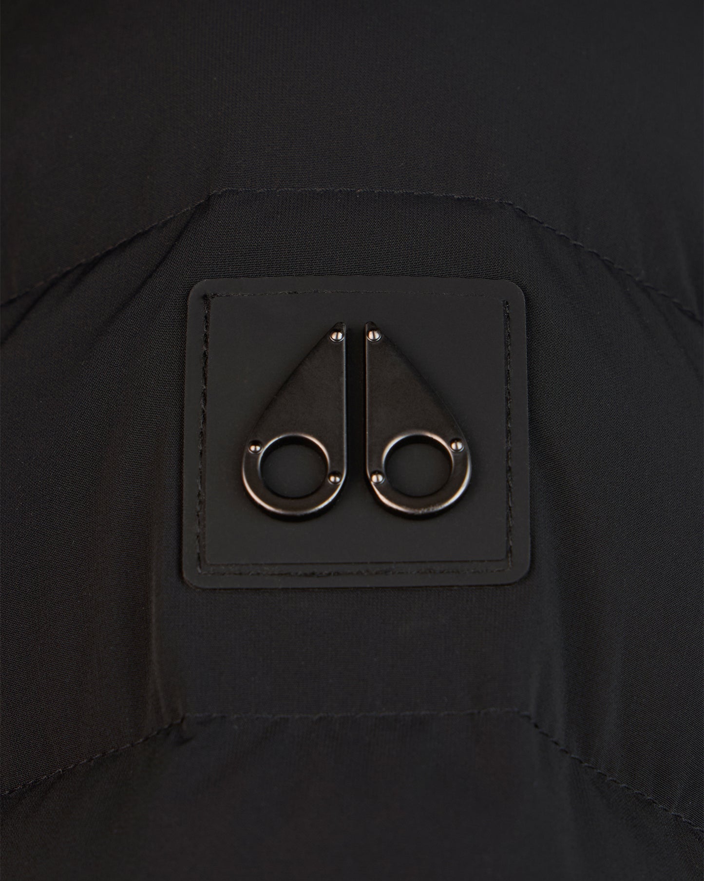 Close-up of a black square patch with a metal logo of two moose silhouettes.