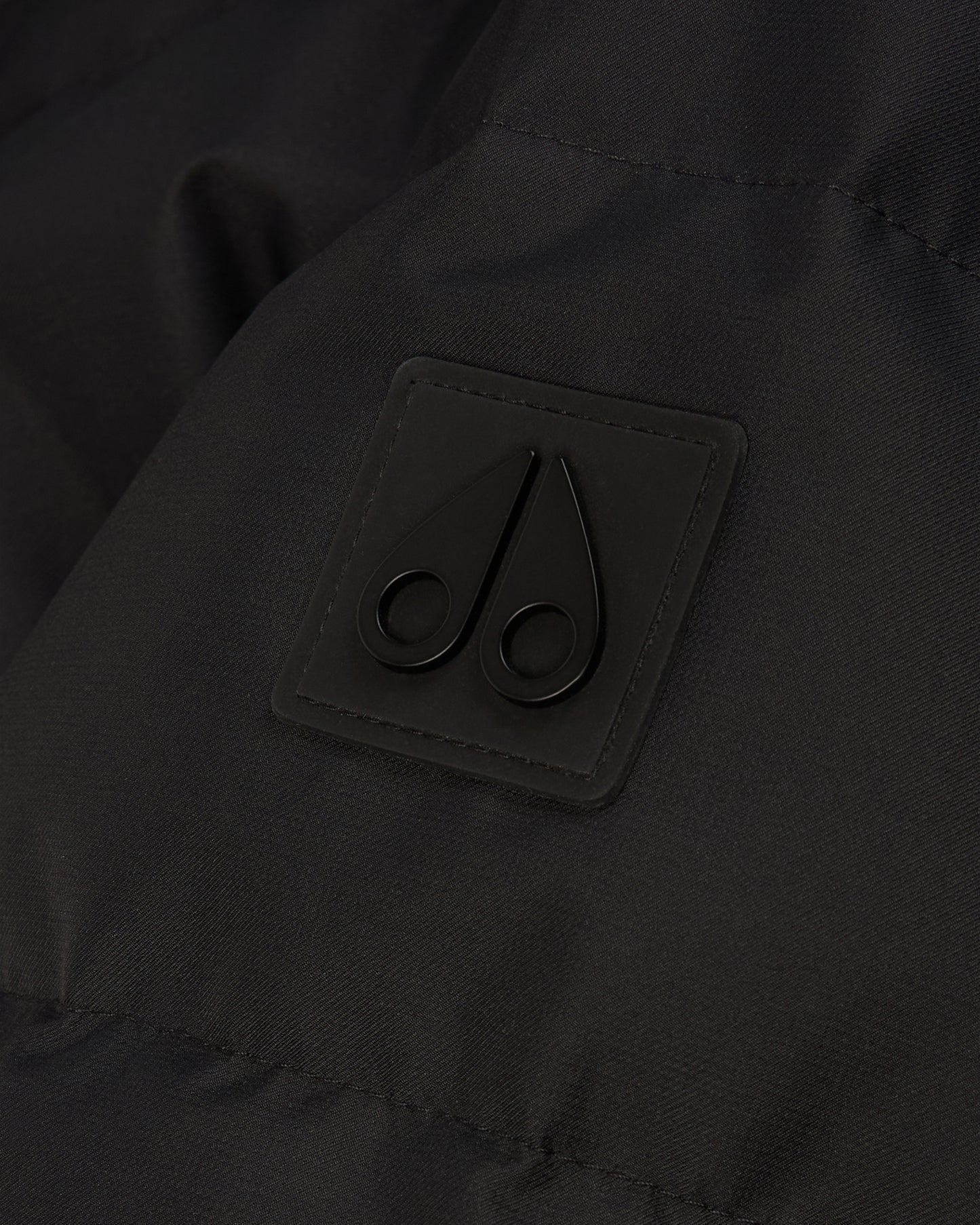 Close-up of a dark garment featuring a small, square patch with a stylized, dark double-scroll logo.
