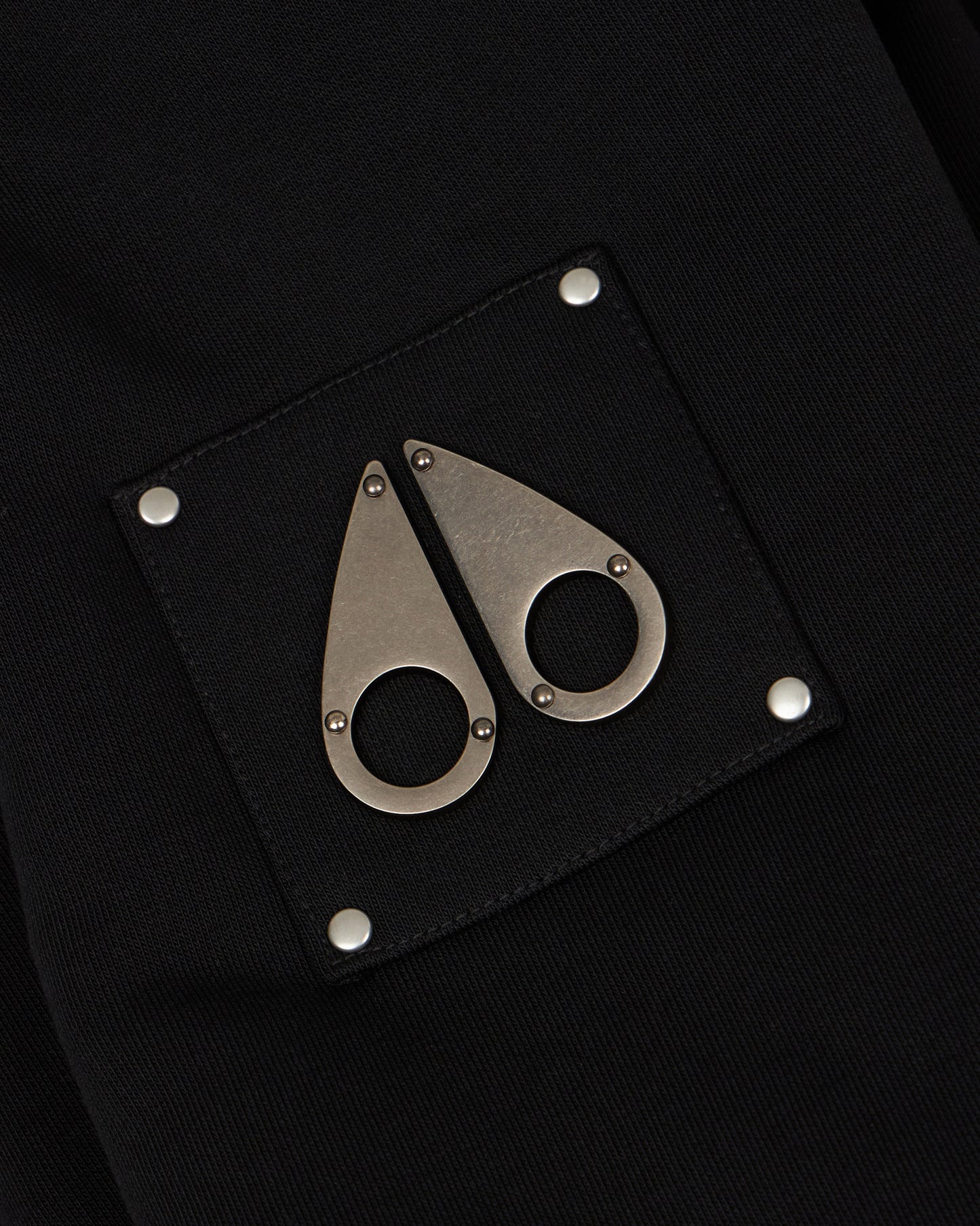 Close-up of a black patch with two metal tear-drop logos, each fixed with a small circular eye.