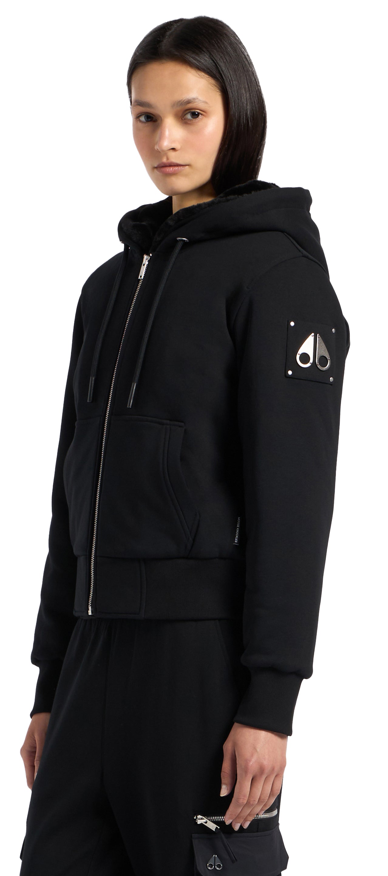 A person wears a black zip-up hoodie with a logo on the sleeve.