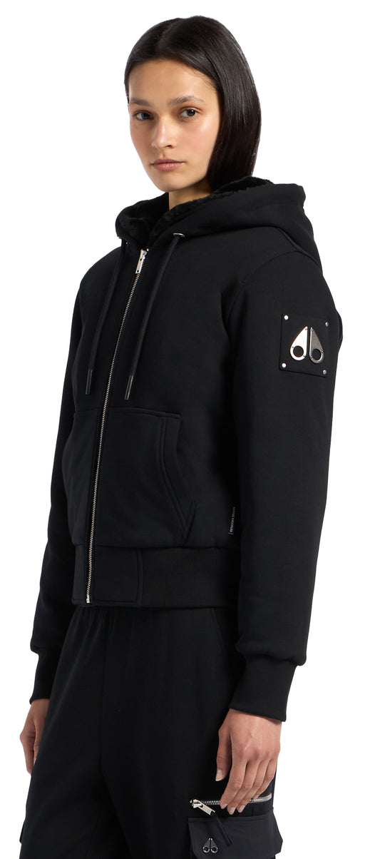 A person wears a black zip-up hoodie with a logo on the sleeve.