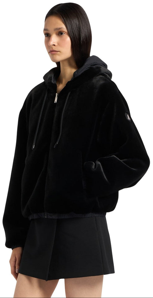 A person wearing a black faux fur hooded jacket with a zipper and two pockets.