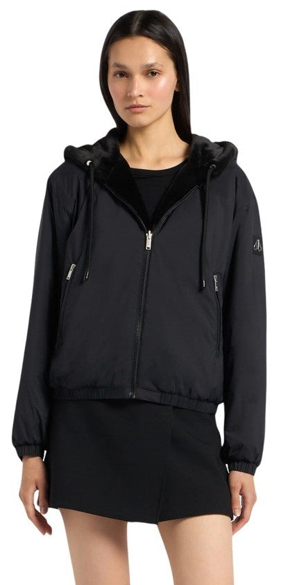 A woman wearing a black hooded jacket and a black skirt.