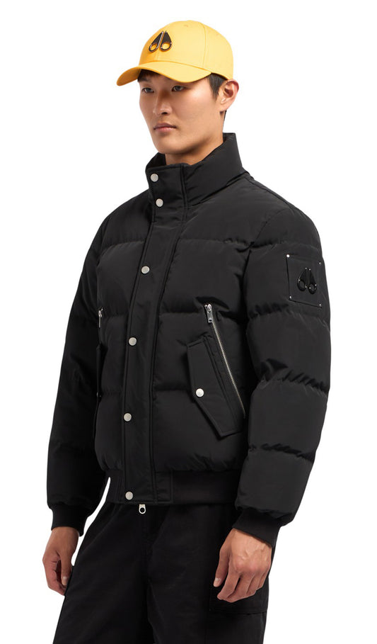 A man in a black puffer jacket and a yellow cap with a moose logo.