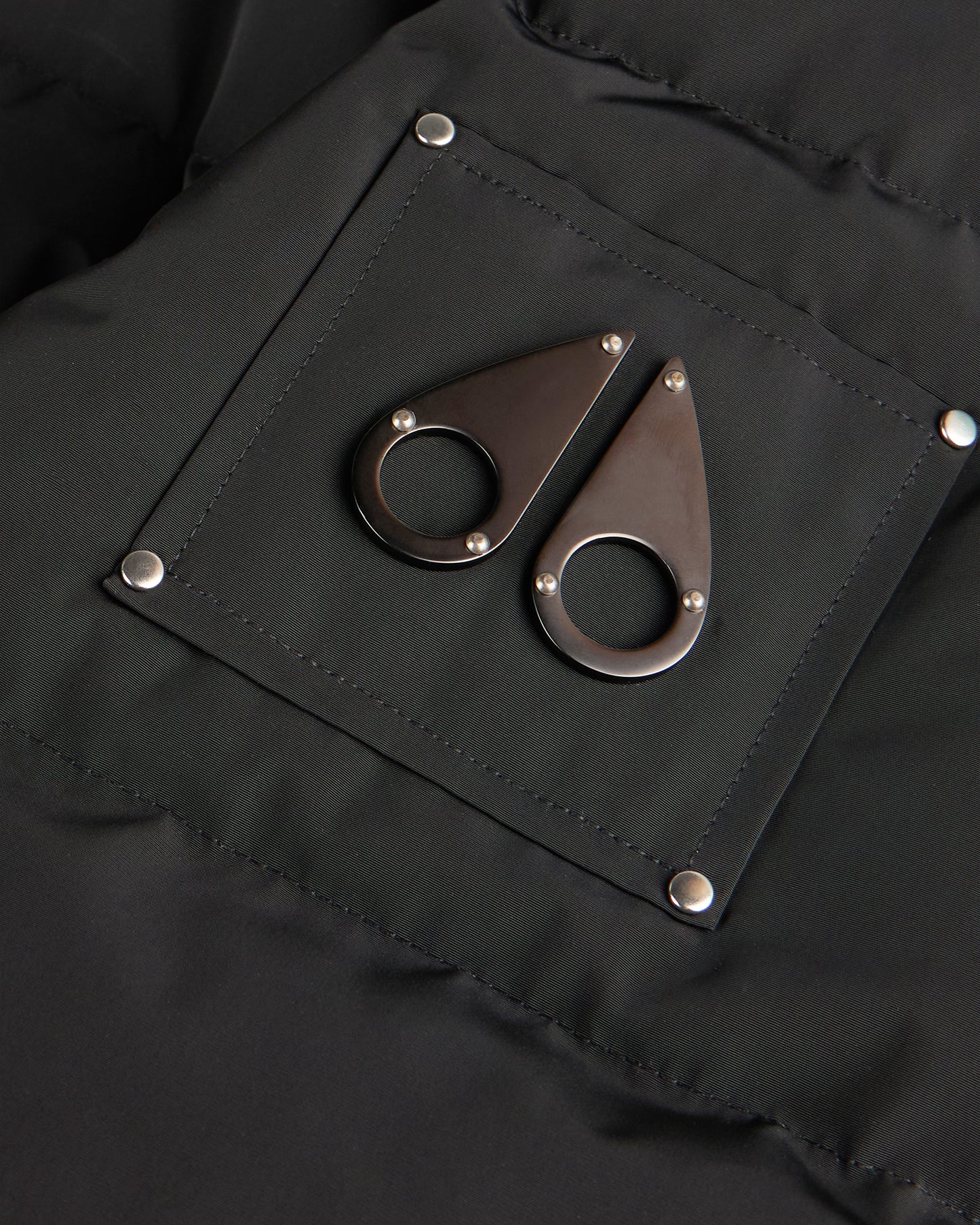 Close-up of a black garment featuring a square patch with rounded metal emblems.