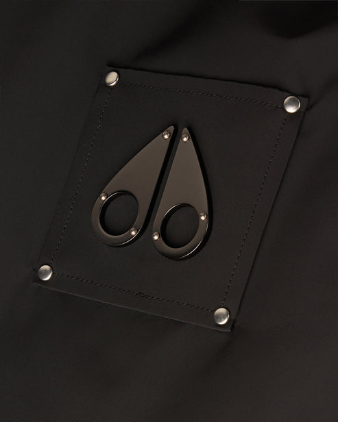 Close-up of a black patch with a metal logo of two teardrop shapes, each with a small ring, attached to a piece of black fabric with silver studs in each corner.