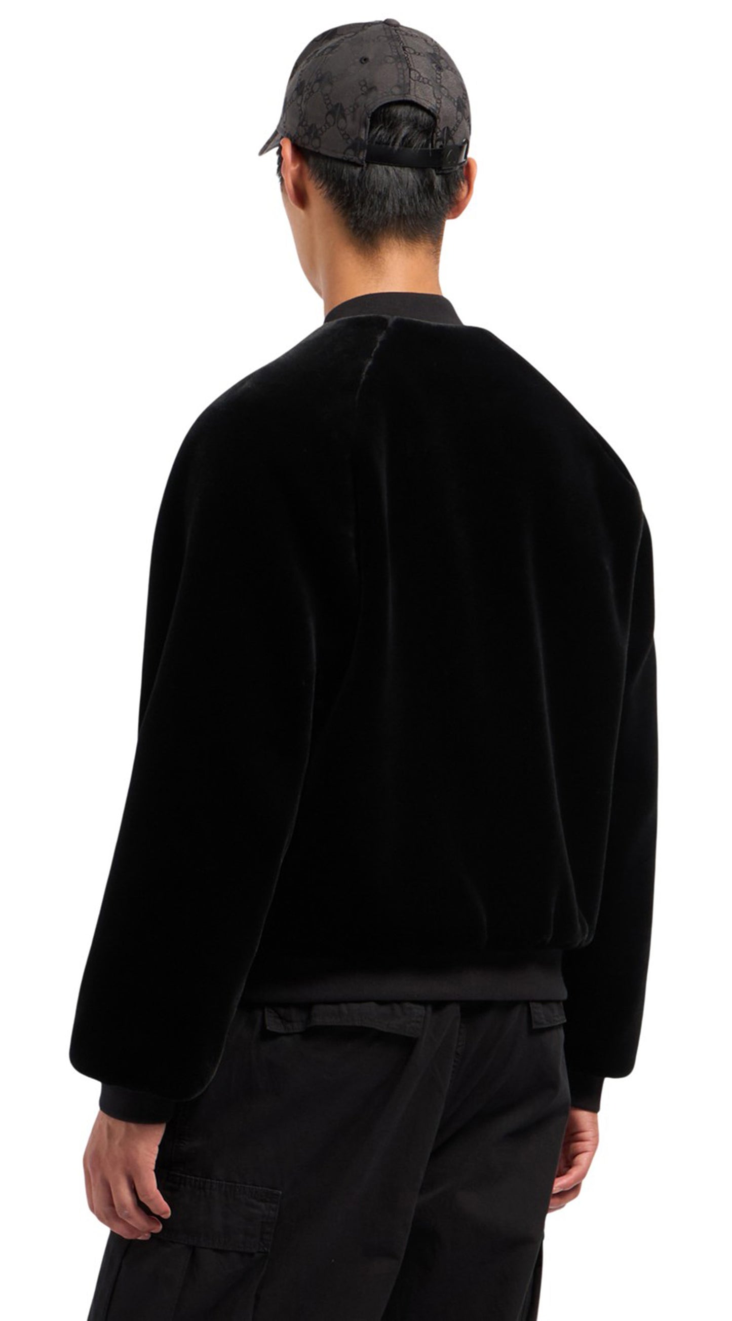 A person wearing a black velvet bomber jacket and a black baseball cap, back view.