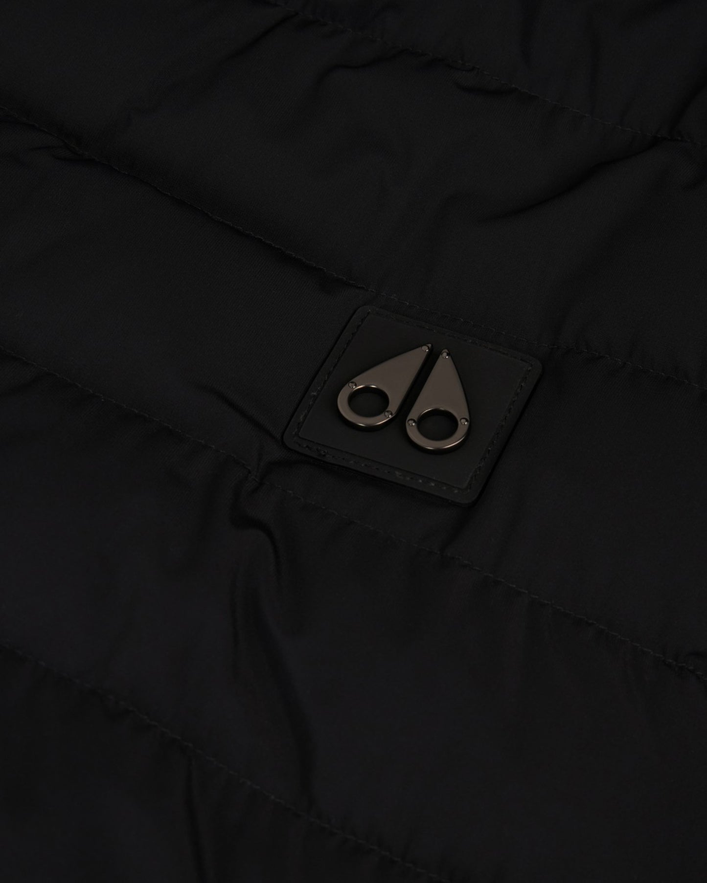 Close-up of black fabric with a small, square tag featuring two metallic, stylized moose knuckles.