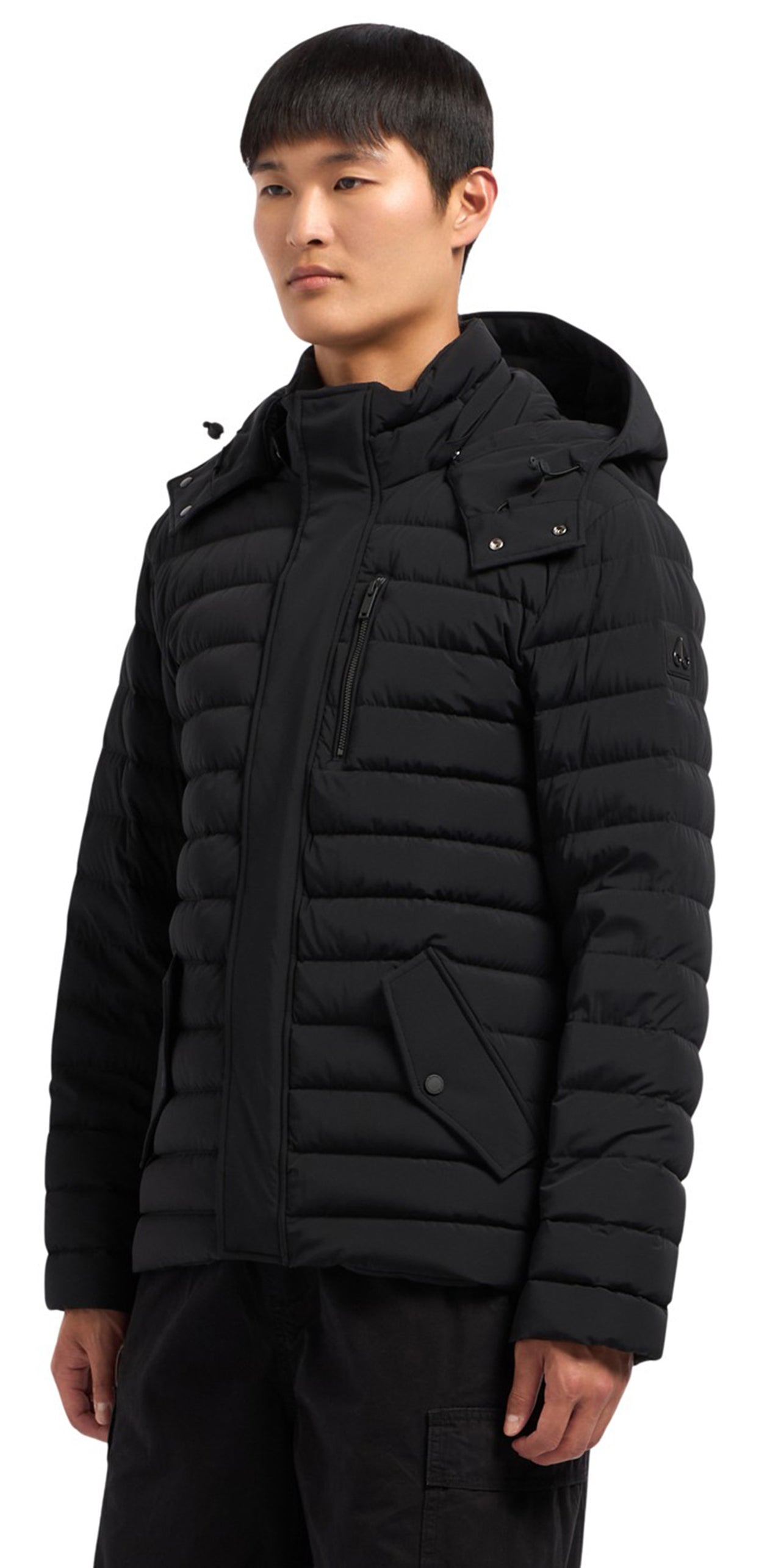 A man wears a hooded, black, quilted puffer jacket with a vertical chest zipper.