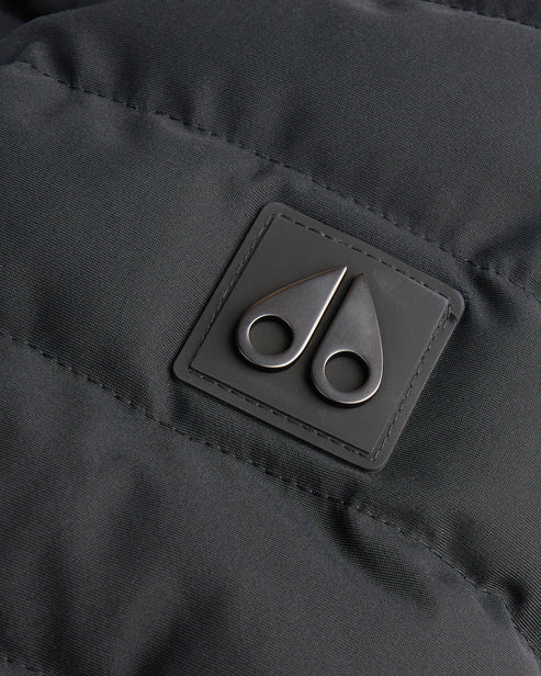 Close-up of the silver-colored logo consisting of two metal cleaver shapes on a dark gray stitched diamond-quilted material.