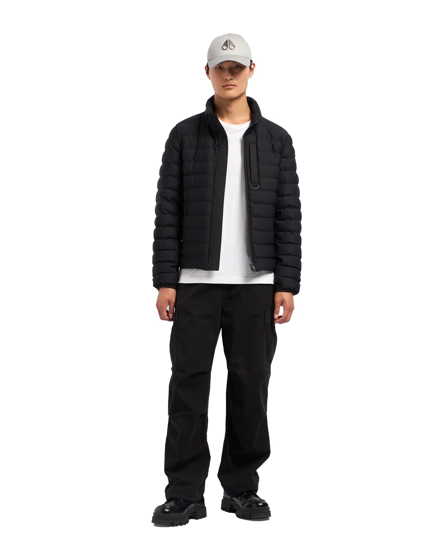 A man stands wearing a black puffer jacket, black pants, and a gray cap.