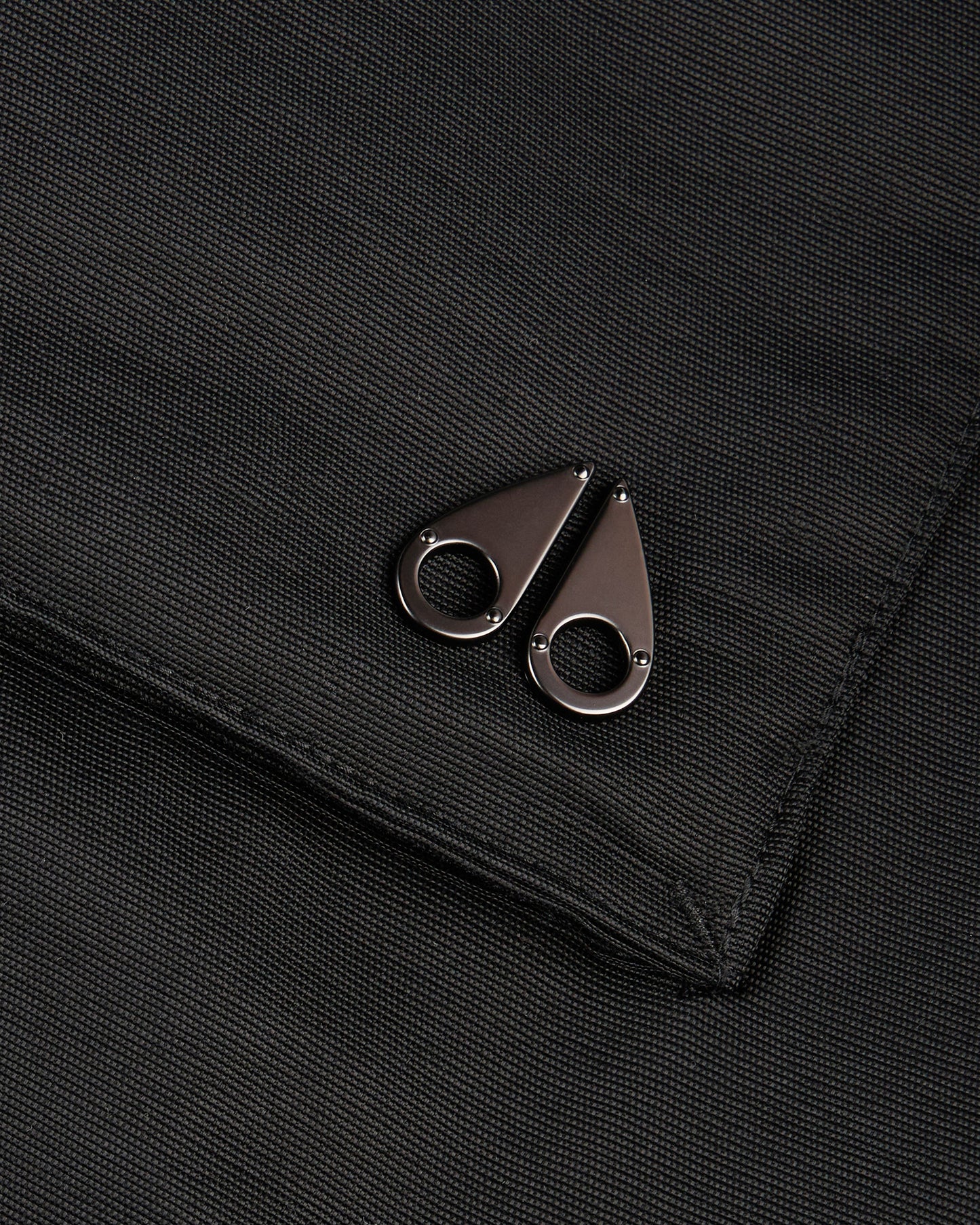 Close-up of a matte, dark gray fabric with two teardrop-shaped metal accents, each having a circular cutout.