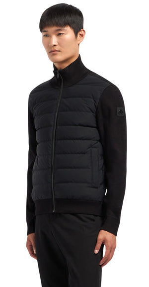 A man models a black quilted vest zipped to the neck with ribbed sweater sleeves.
