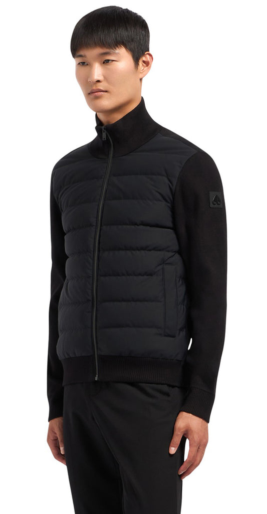 A man models a black quilted vest zipped to the neck with ribbed sweater sleeves.