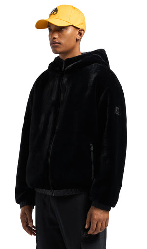 Man wearing a yellow cap and a black, furry zip-up hooded jacket.