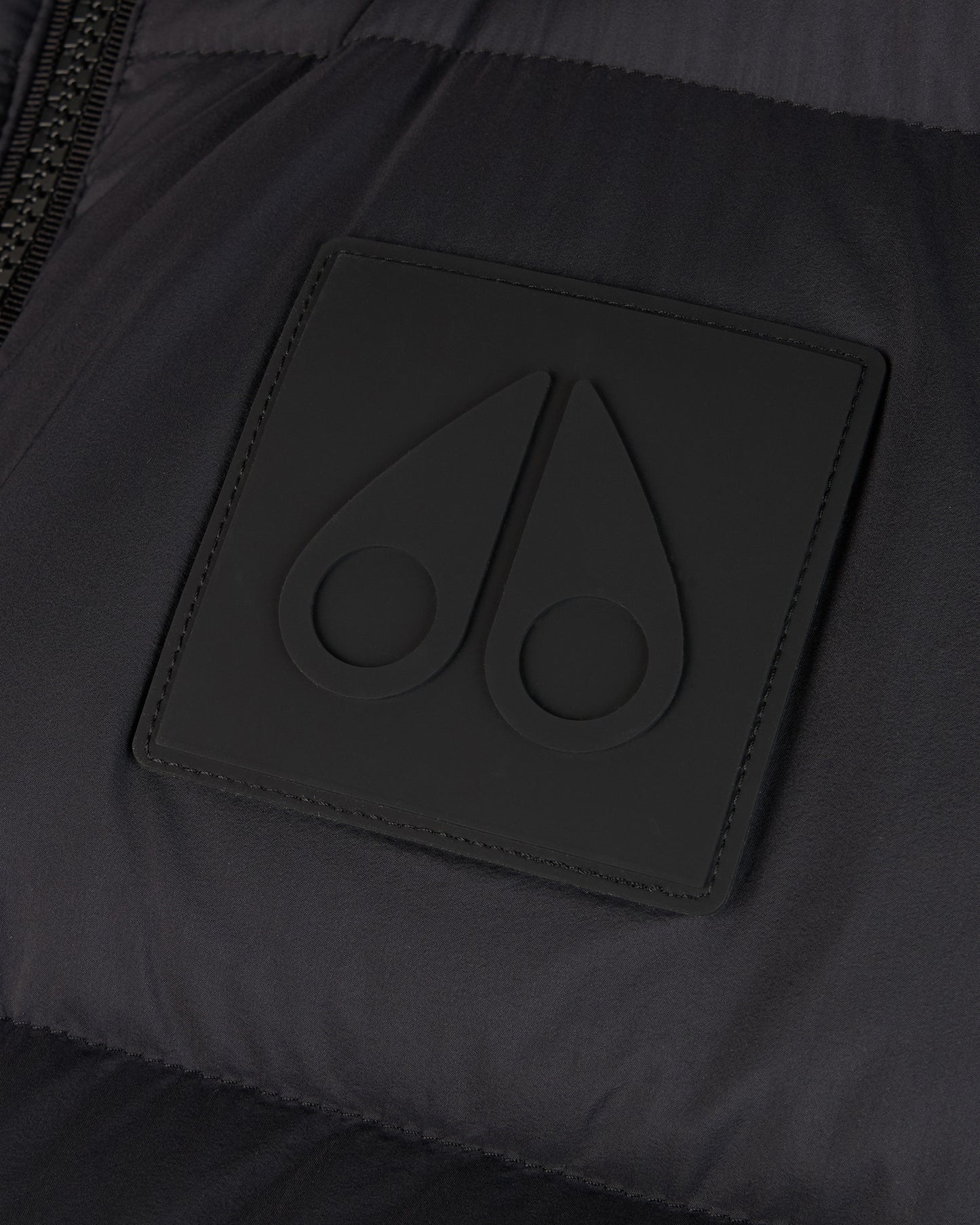 Close-up of a dark square patch with a subtle, raised emblem featuring two teardrop shapes with circular indents.