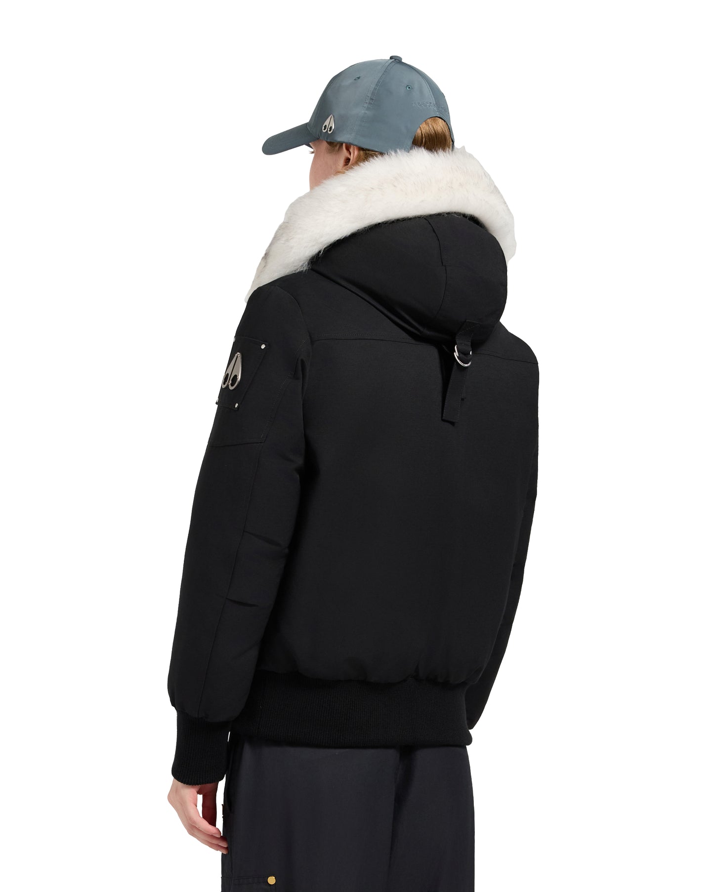Back view of a black bomber jacket with a white fur-trimmed hood, black ribbed cuffs and waistband, and a logo patch on the left sleeve.