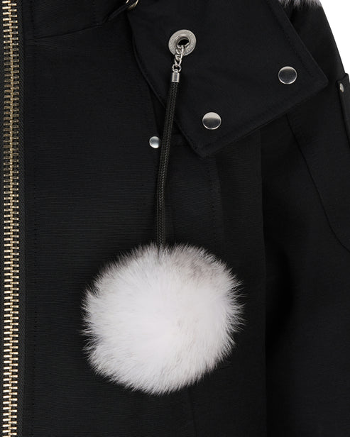 Close-up of a black coat with a detachable white fur pom-pom attached to the hood.