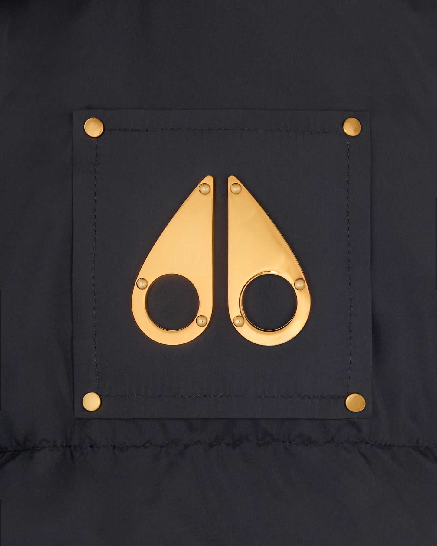 Gold metallic moose knuckle logo on dark fabric.