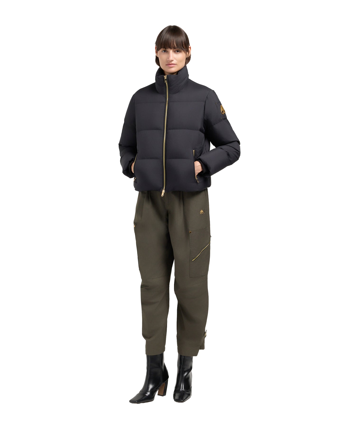 A person wearing a black puffer jacket, olive green pants and black boots, standing.