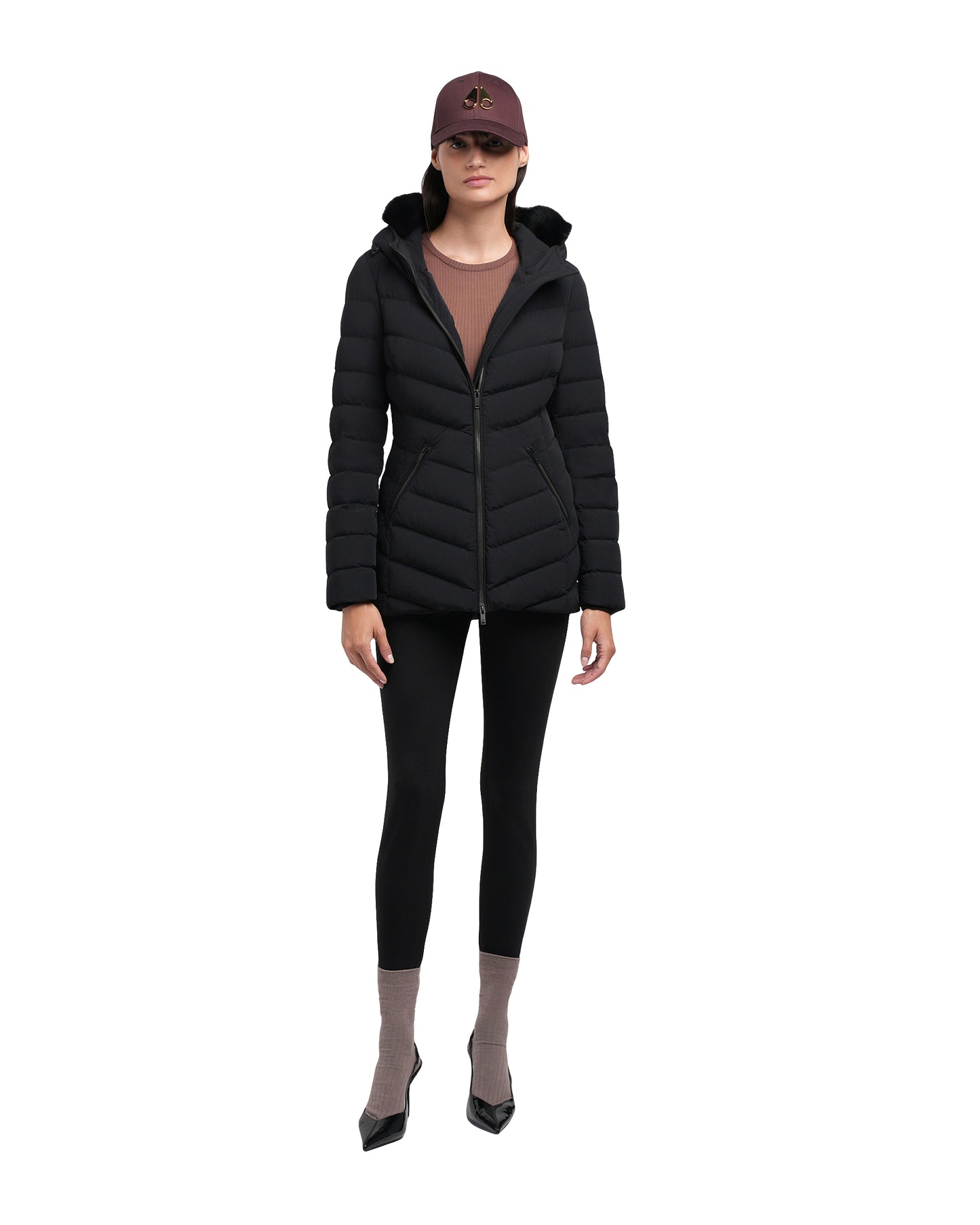 Woman wearing a black quilted hooded puffer jacket, black leggings, taupe socks, and black heels.