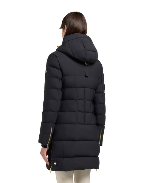 Back view of a woman wearing a black quilted parka with a hood and gold zippers.