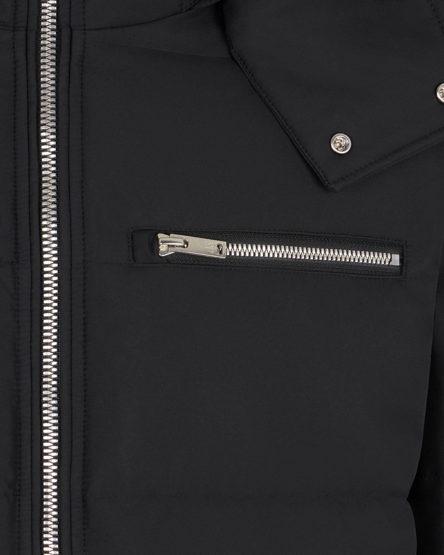 Close-up of a black jacket, focusing on a silver zipper detail on a chest pocket and the jacket's main zipper.