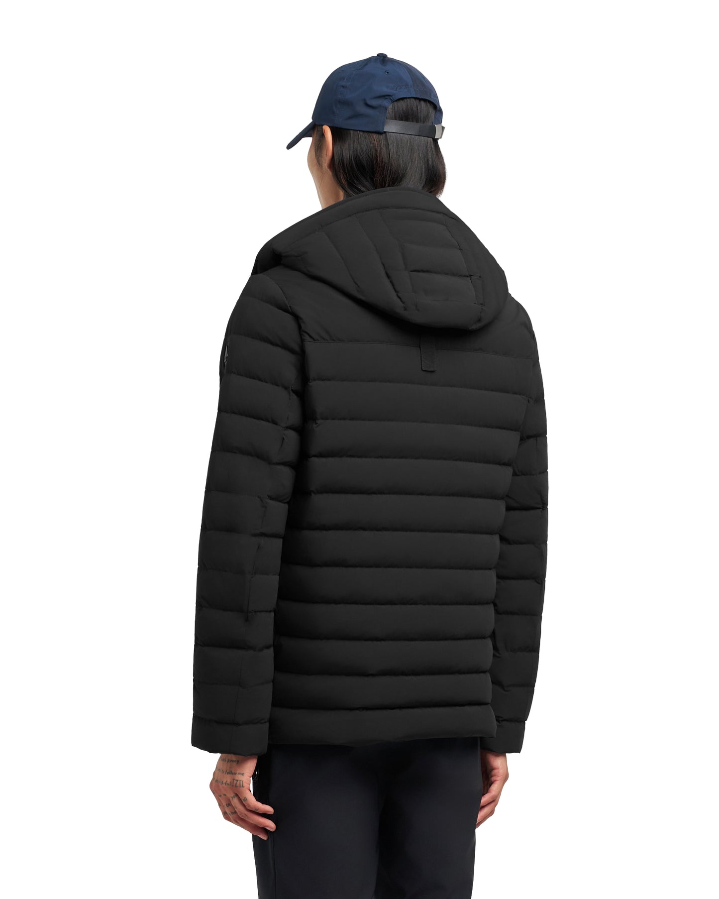 Person facing away wearing a black hooded puffer jacket and navy blue baseball cap.