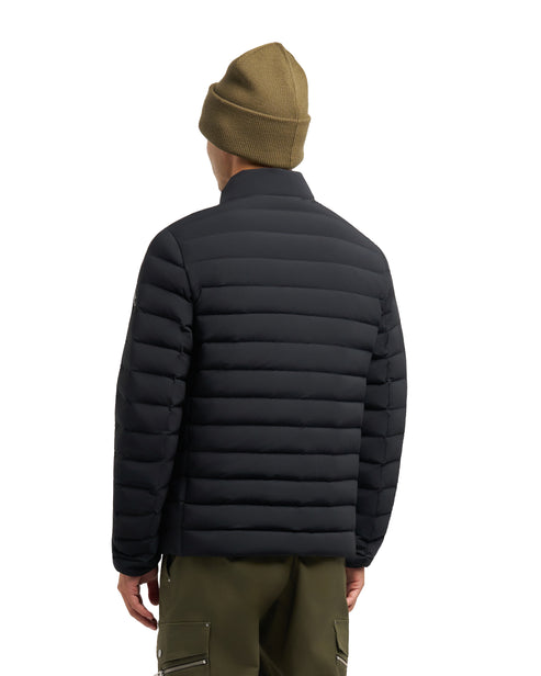 A man is wearing a black puffer jacket, dark olive green pants, and a beanie; back view.
