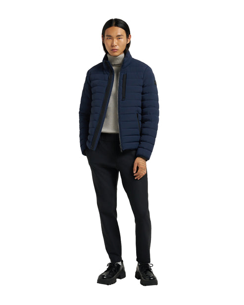 A man in a navy puffer jacket, gray turtleneck sweater, black pants, and black shoes.