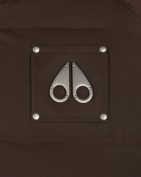 Close up of a brown fabric with metal logo, a square patch with two metal pieces that look like moose knuckles attached with silver rivets.
