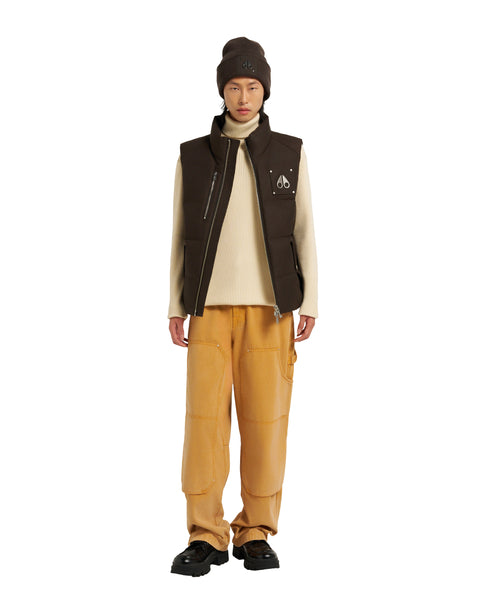 A person wearing a brown knit cap, a tan turtleneck sweater, a brown vest, and khaki pants. They also wear black shoes.