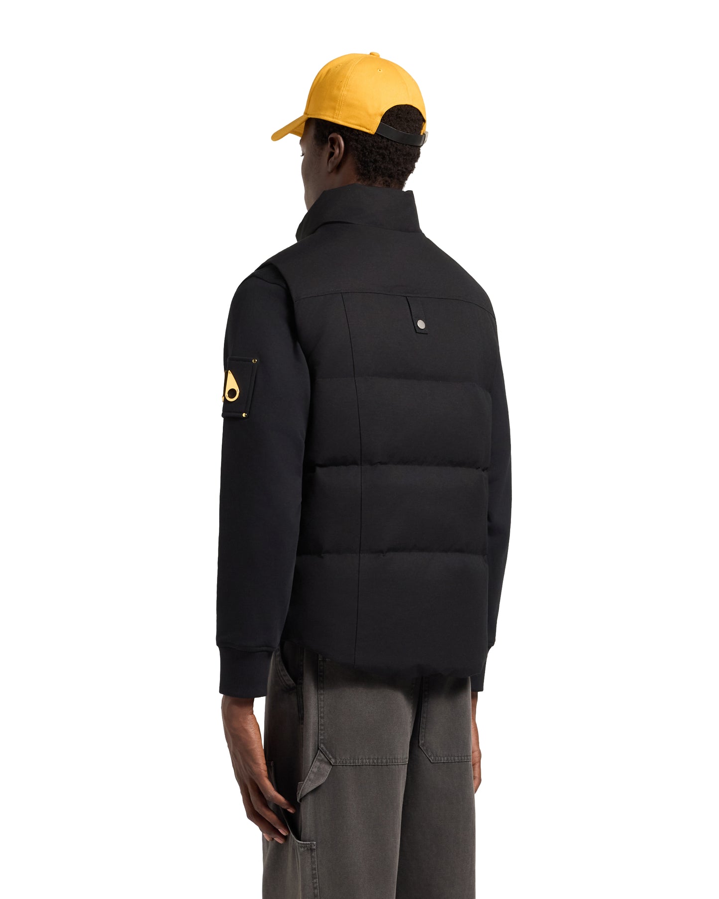 A person wearing a black padded vest, black sweatshirt, gray pants, and yellow hat, viewed from the back.