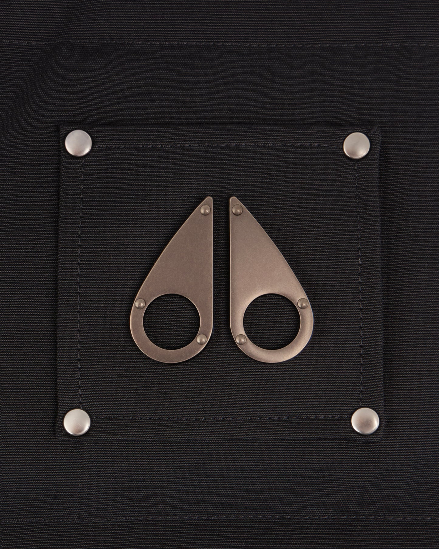 Close up of a black patch on clothing with two silver moose knuckle-shaped decorations attached with silver rivets.