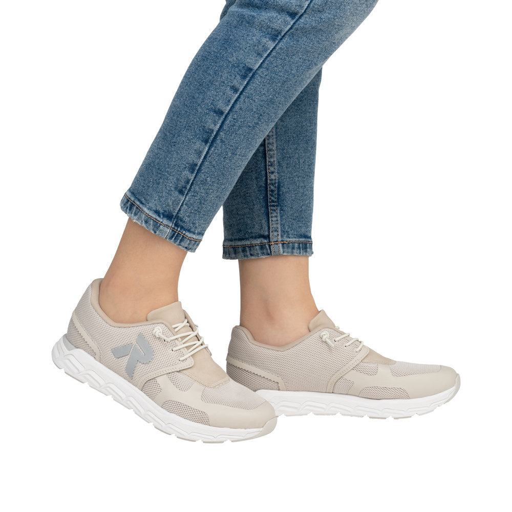 A person in jeans wearing beige sneakers with white soles.