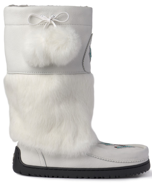 A tall white leather winter boot with a thick white faux fur shaft, a white drawstring tie with two fluffy white pom-poms near the top, and a sturdy black rubber sole, featuring subtle embroidered detail on the toe.