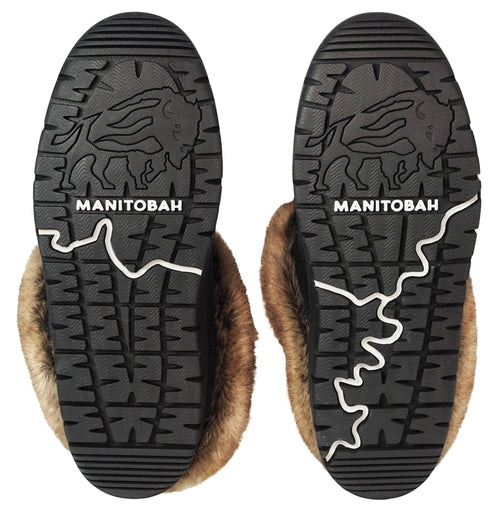 The black rubber outsoles of two winter boots, each featuring an embossed bison graphic, the word MANITOBAH in white text, and a decorative white line, with brown fur lining visible around the edges.