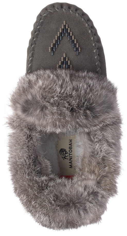 A gray suede moccasin-style slipper seen from above, featuring a decorative bead pattern on the toe and a thick, fluffy gray faux-fur lining that surrounds the opening, with a visible product label inside reading MANITOBAH.