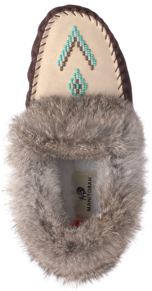 A tan suede moccasin with fluffy gray faux fur trim around the opening, featuring a geometric bead pattern in teal, white, and brown on the toe, with a 'MANITOBAH' label visible inside.