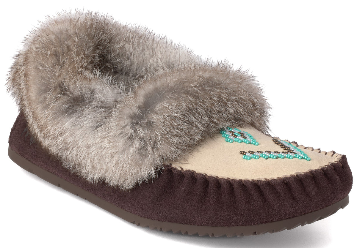 A brown suede moccasin slipper featuring a cream-colored top panel adorned with turquoise beadwork and a fluffy gray fur-trimmed collar.