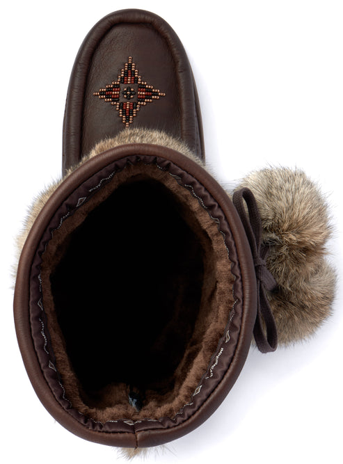 A top-down view of a dark brown suede winter boot with a soft, dark brown fur lining. The toe of the boot features a decorative geometric pattern stitched with small colored beads. The upper part of the boot is trimmed with a band of fluffy light brown faux fur and a decorative bow with pom-poms on the side.