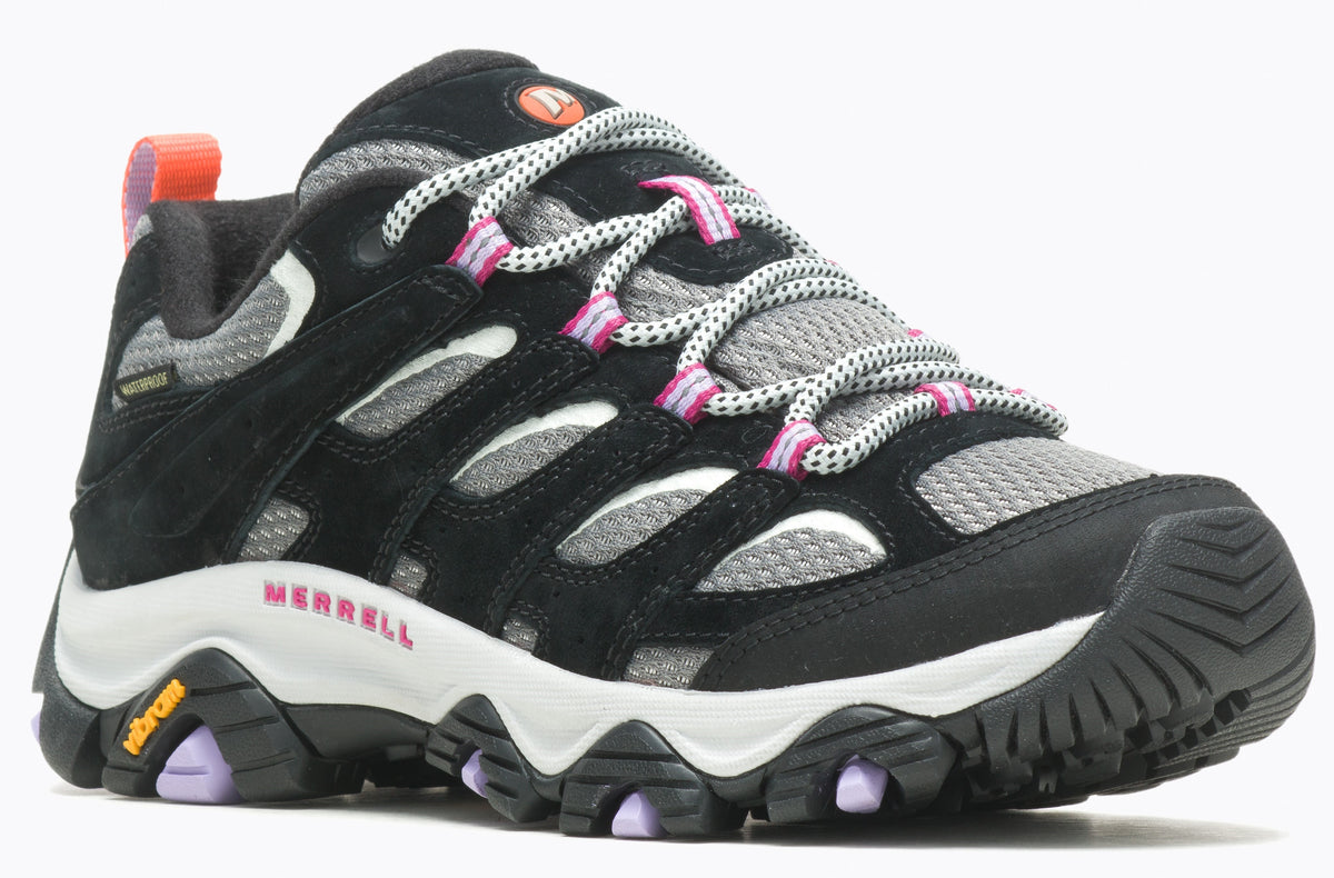 A black and gray hiking shoe with Vibram sole, featuring pink accents on the eyelets and a Merrell logo.