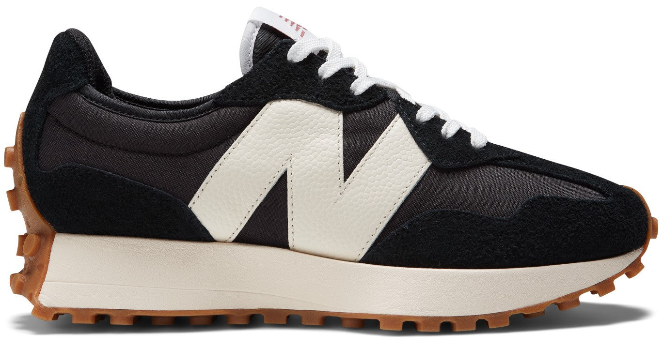 A black and white New Balance 327 sneaker with a prominent oversized white N logo on the side, a thick cream-colored midsole, and a signature lugged gum-rubber outsole extending up the heel.