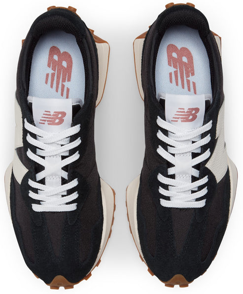 A pair of black and cream New Balance 327 sneakers seen from a top-down view, featuring white laces, brown lugged soles, and the New Balance logo in pink on the tongue and insole.