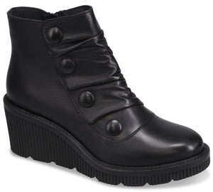 A black ankle boot with a rounded toe, a high wedge sole with a ribbed texture, and decorative buttons running diagonally up the side, which also features subtle ruching.