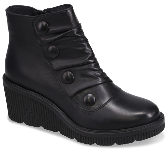 A black ankle boot with a rounded toe, a high wedge sole with a ribbed texture, and decorative buttons running diagonally up the side, which also features subtle ruching.