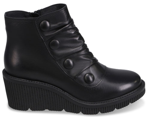 A black leather wedge-heeled ankle boot with a rounded toe, a side zipper, and a decorative panel featuring four matching black buttons, set against a black, heavily ridged wedge sole.